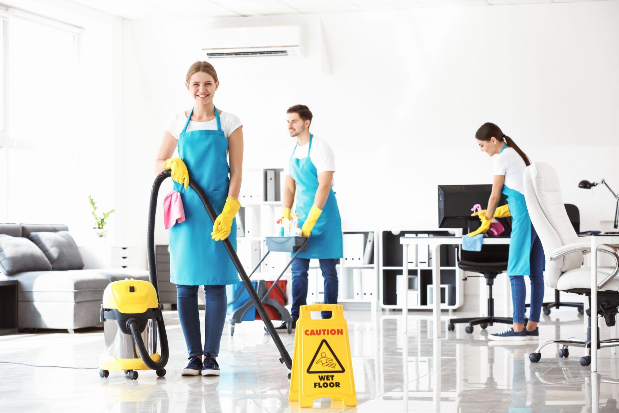Três pessoas uniformizadas realizando a limpeza de um escritório.