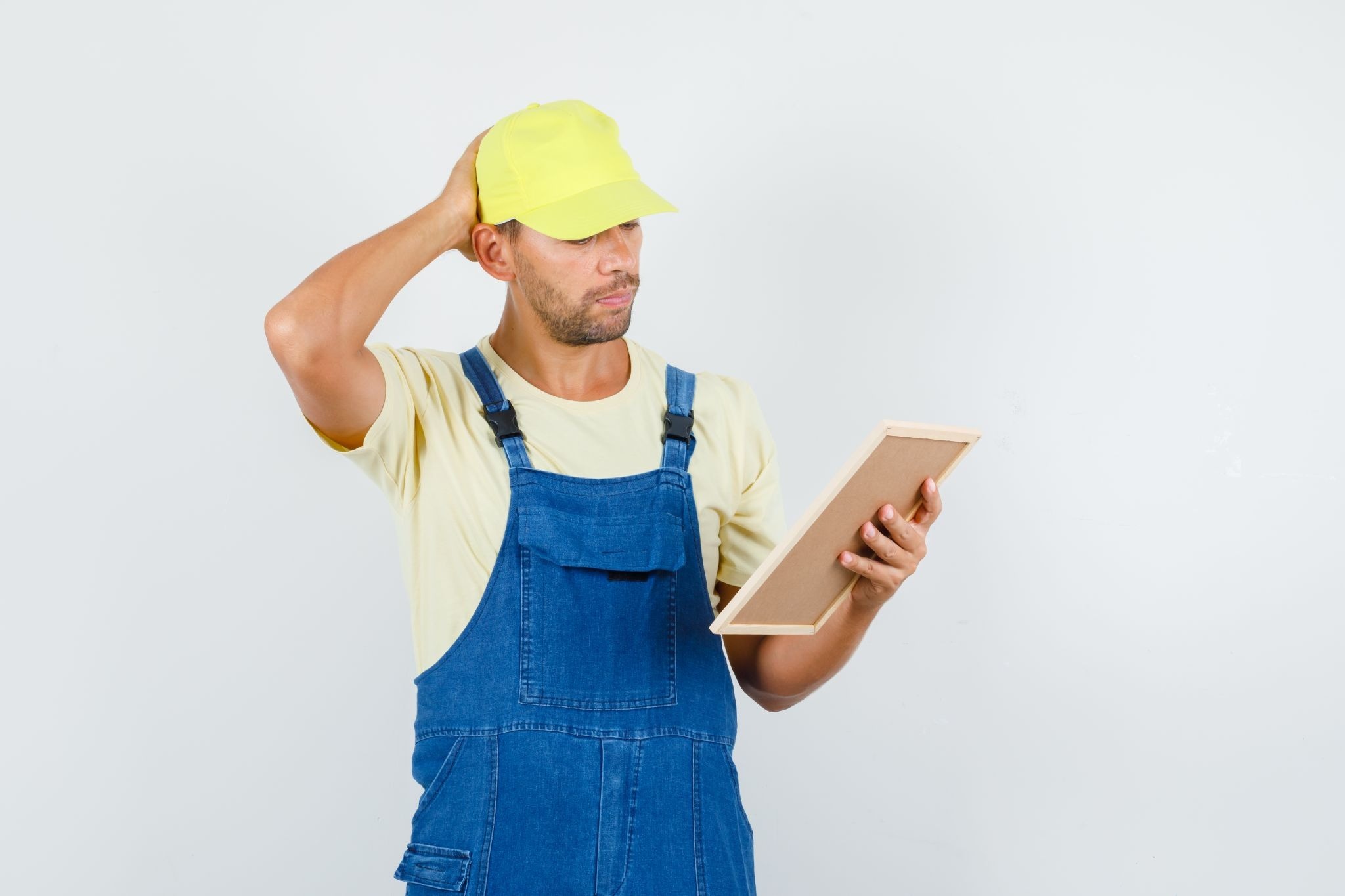 Um homem com roupa de trabalho olhando uma prancheta com olhar questionador.